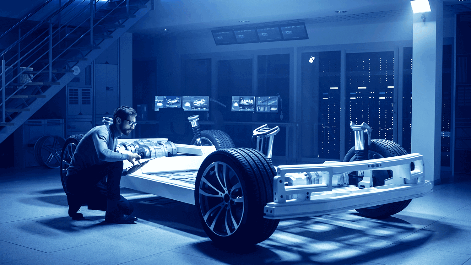 A technician in a sleek modern lab kneeling by a modern electric vehicle chassis.